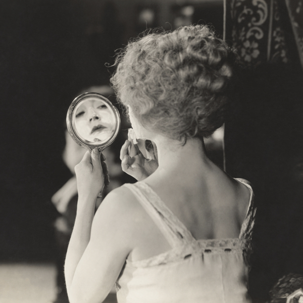 Woman looking at the mirror while putting on her face a cream with urea, the best moisturiser for skin of all ages.