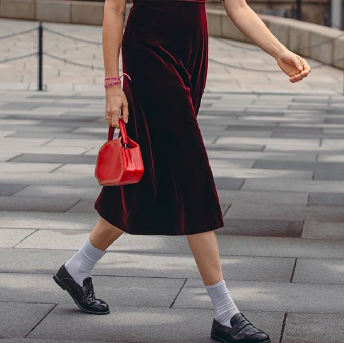 Veronika Heilbrunner attending a runway show at Paris Fashion Week, wearing red velvet dress and white socks with loaefers