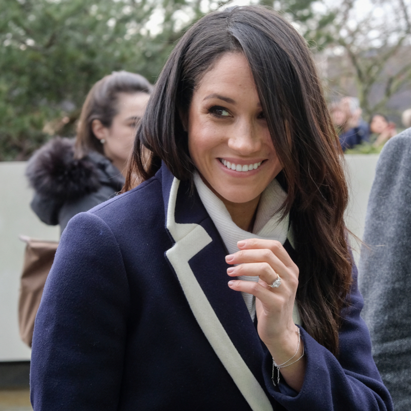 A smiling Meghan Markle in a black and white jacket and white turtleneck.