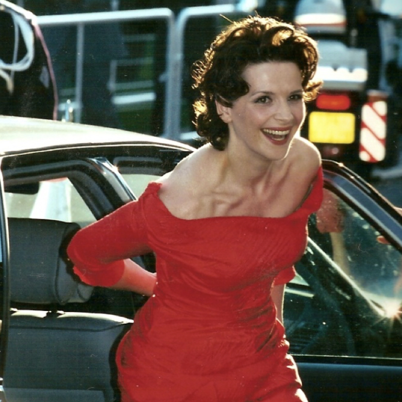 French actress Juliette Binoche smiling in a red dress.
