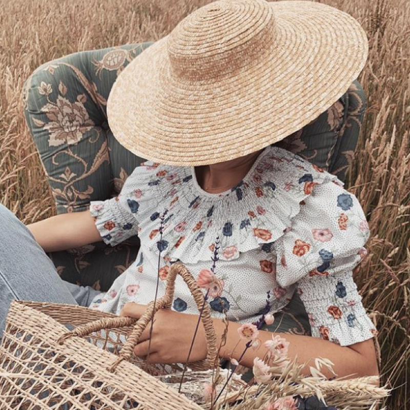 Woman wearing a floral shirt from the made-to-order fashion label Andion and a large straw hat.