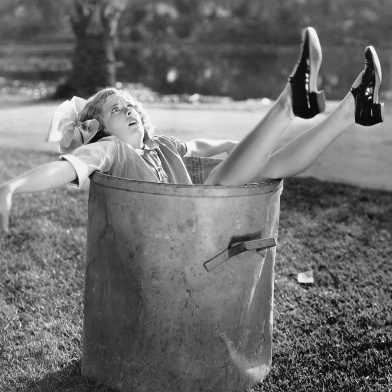 Woman in a trash can, overwhelmed by added stress of self-care routine.