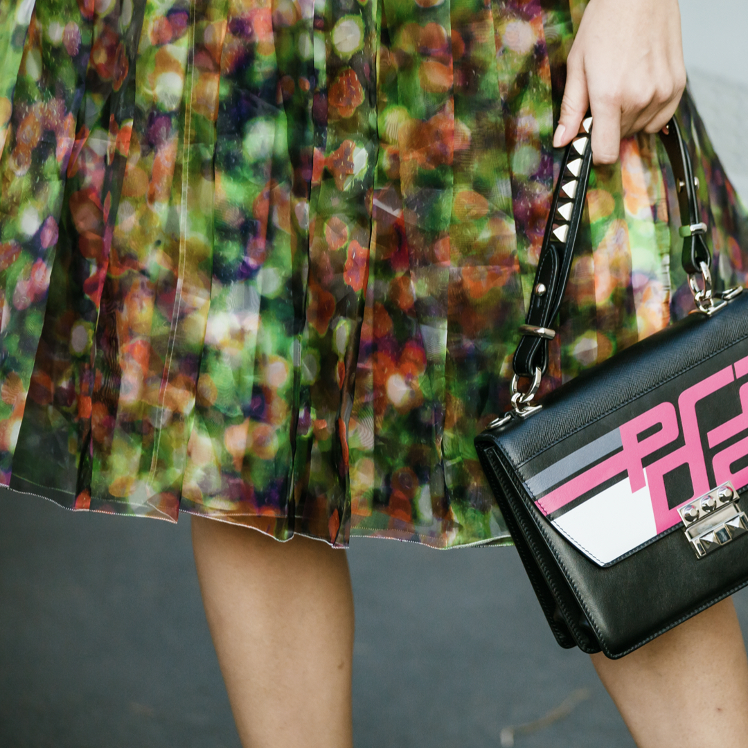 detail of a pleated floral skirt and a prada bag from street style milan fashion week