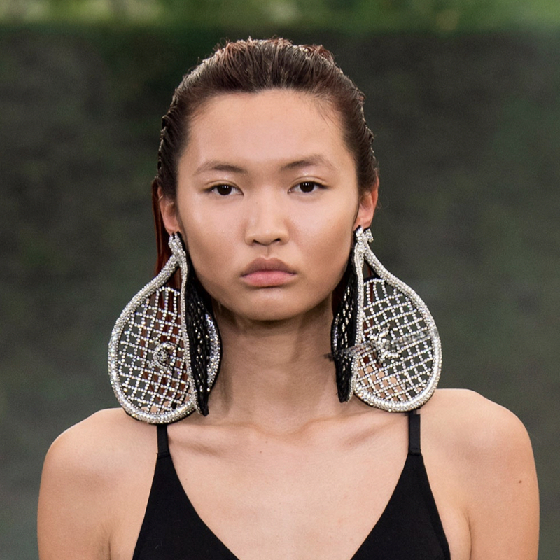 Model wearing tennis racket earrings and sportswear.