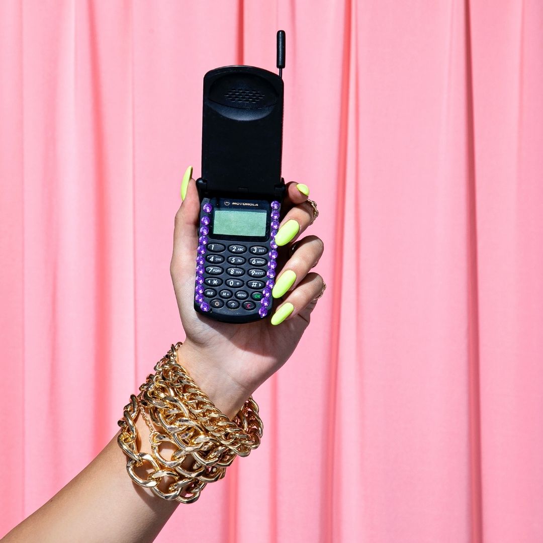 detail of a hand holding an vintage mobile phone, wearing a yellow neon nail polish