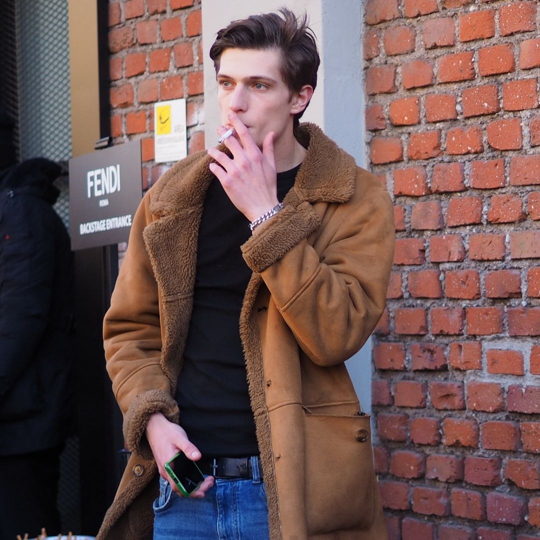 Street style of a man smoking outside Fendi runway, wearing a lambskin coat