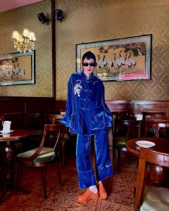 fashionista and vintage expertJudith Bradl in a coffee shop in south tirol wearing a blue velvet chinese emsemble and orange clogs from Melissa 