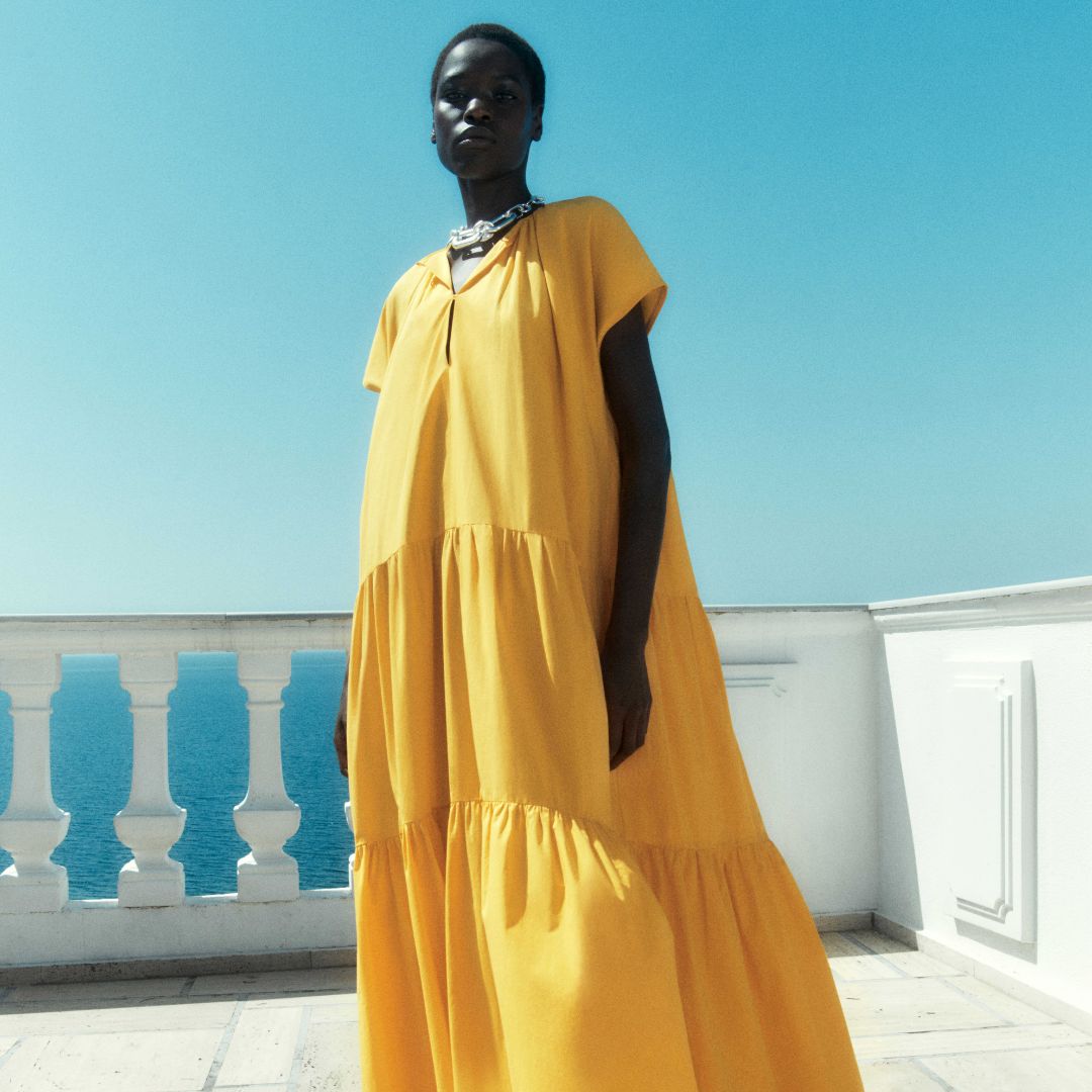 model wearing a roomy yellow dress on a terrace against a blue sky