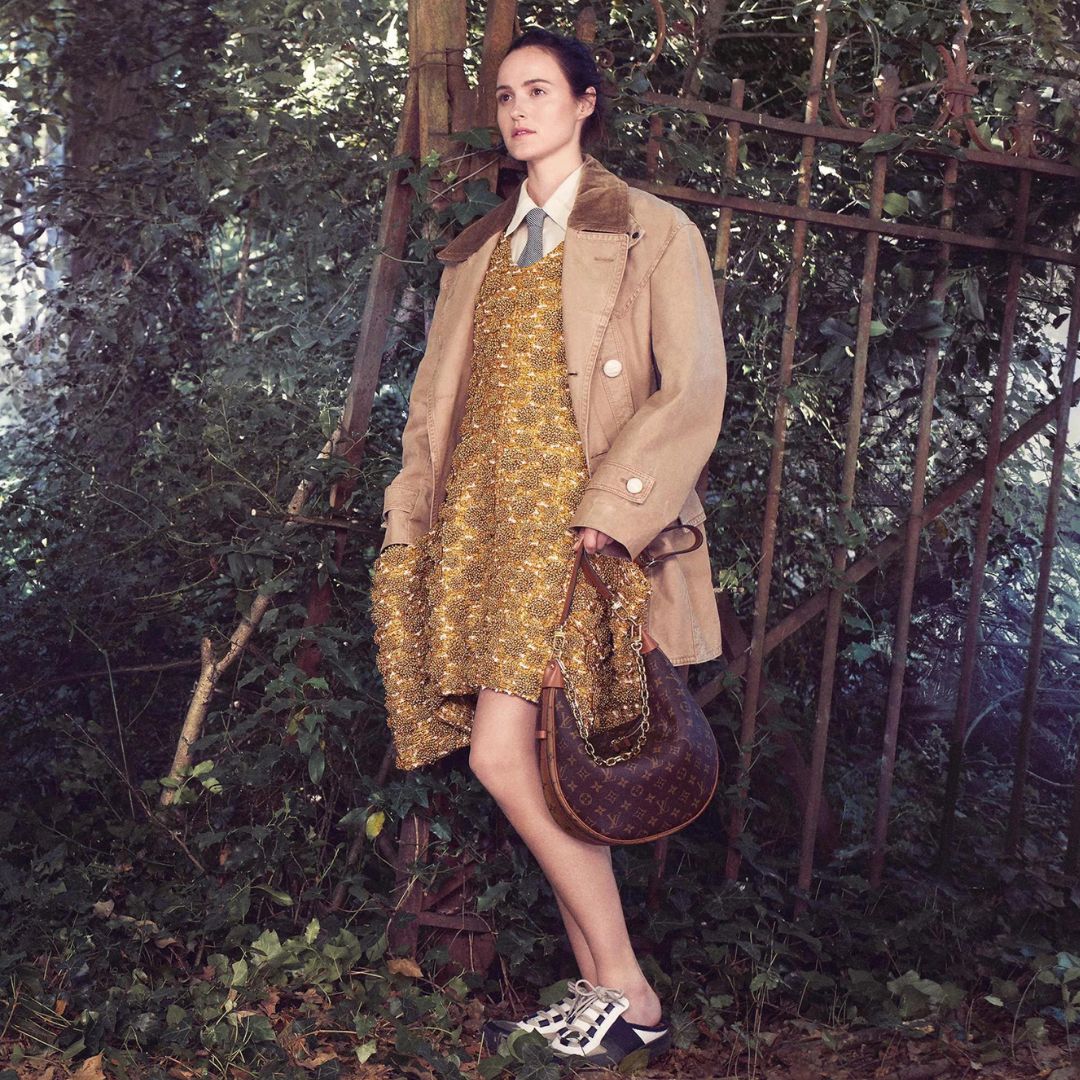 Louis Vuitton AW 22-23 photographed by Davis Sims shows model in a forest wearing a trenchcoat, gold dress and a monogramed bag