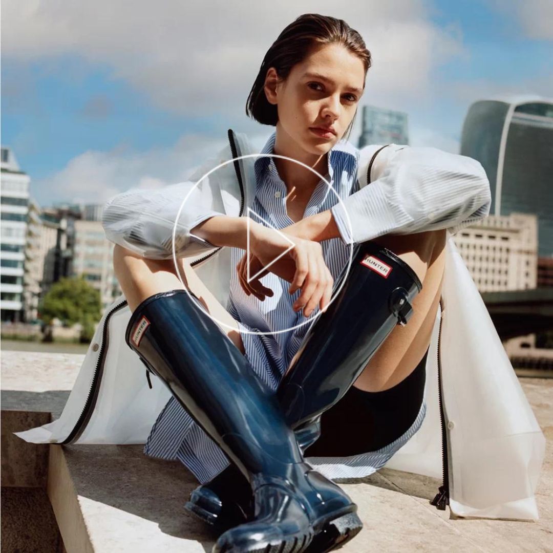 Hunter model sitting on the roof top wearing a transparent rain coat and a rubber boot