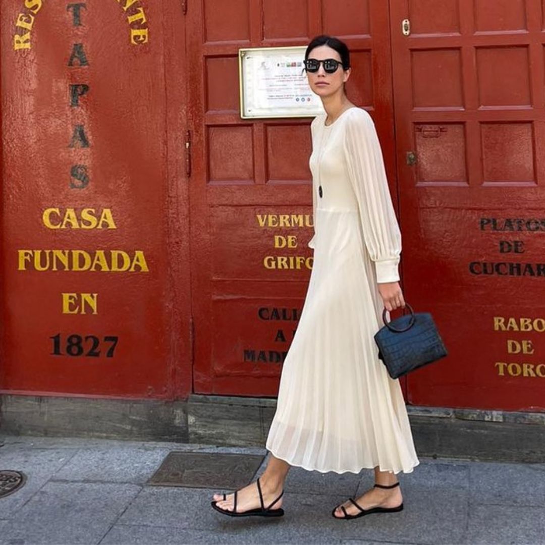 Alessandra de Osma or Princess Alessandra of Hannover walking through the streets of Madrid, wearing a white dress and carrying a bag from her brand Moi and Sass.