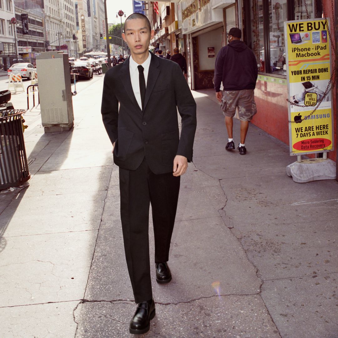 street style photo of a model walking in a busy street wearing a COS dark suit with tie and white shirt