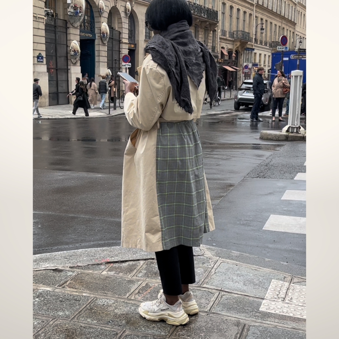 street style photo in Paris, where a woman waits to cross the street wearing a trench coat with a plaid detail on her back