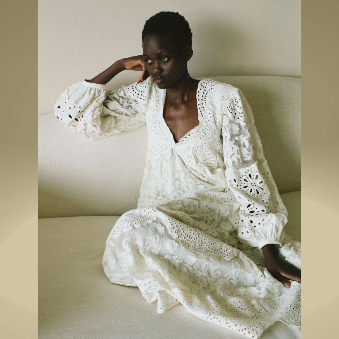A model sitting in a beige sofa, wearing a embroidered maxi white dress from Sea New York