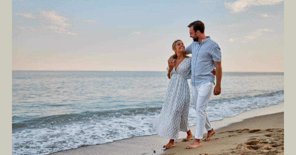 couple walking on the beach wearing a matching outfit in white and blue.