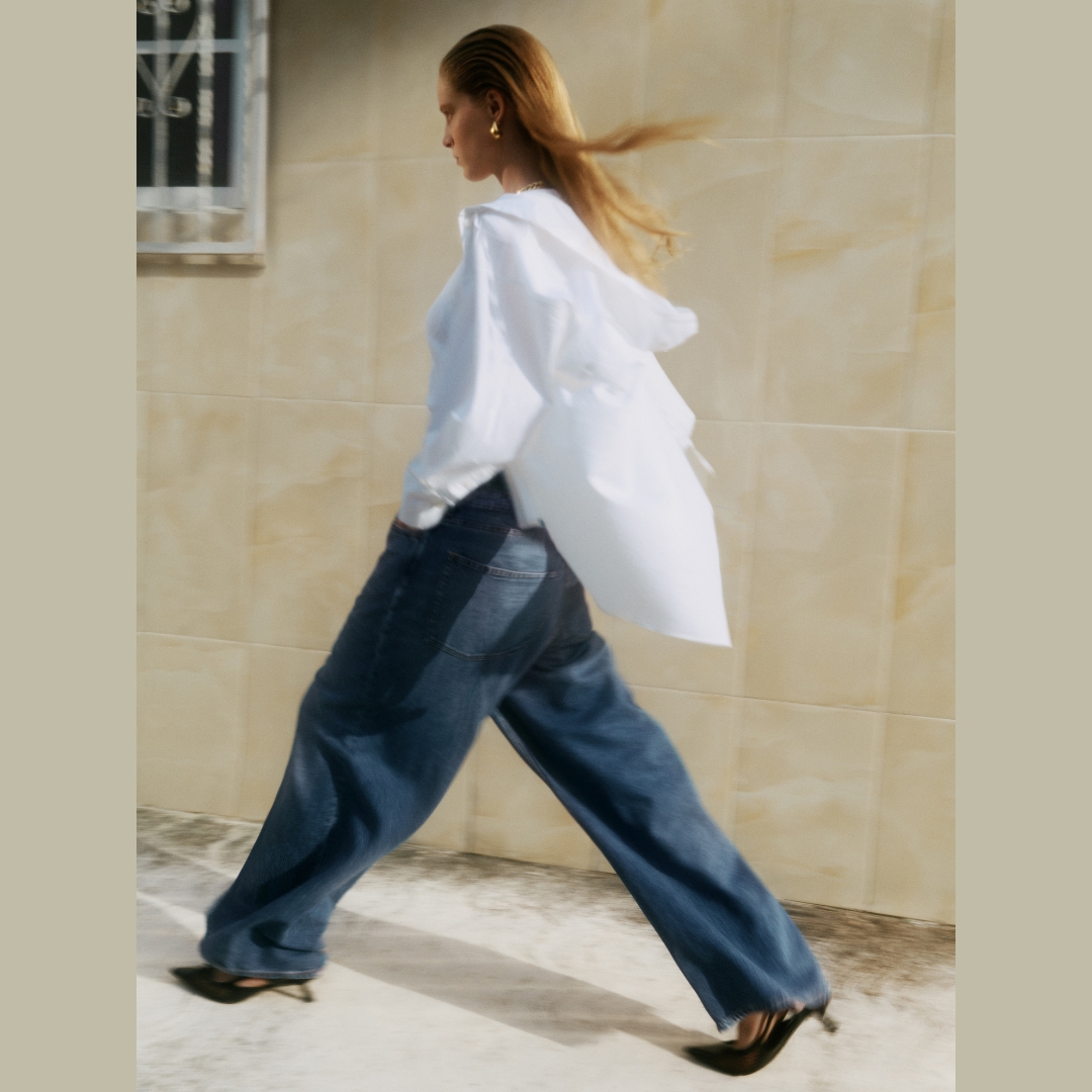 COS model walking in a street wearing a wide leg dark denim paired with a white shirt- denim trends 2024