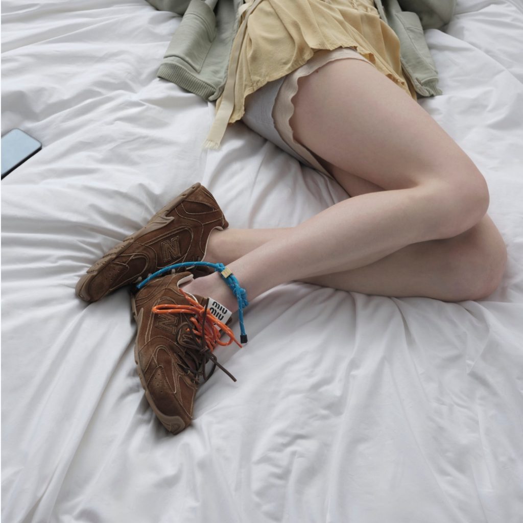 Detail of a model lying on a bed wearing shorts and miu miu sneakers in collaboration with New Balance