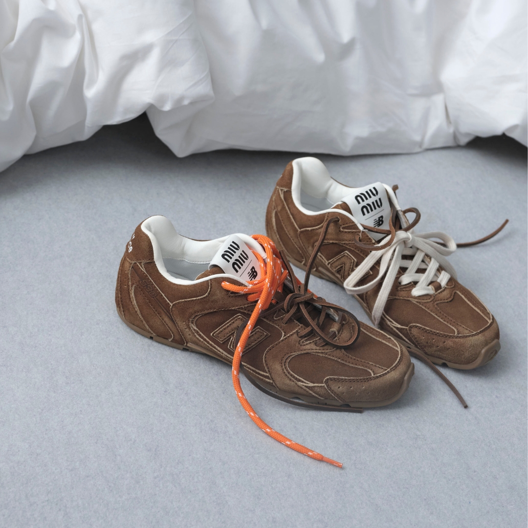 A pair of Miu Miu SS24 sneakers in collaboration with new balance, stays on the floor beside a bed