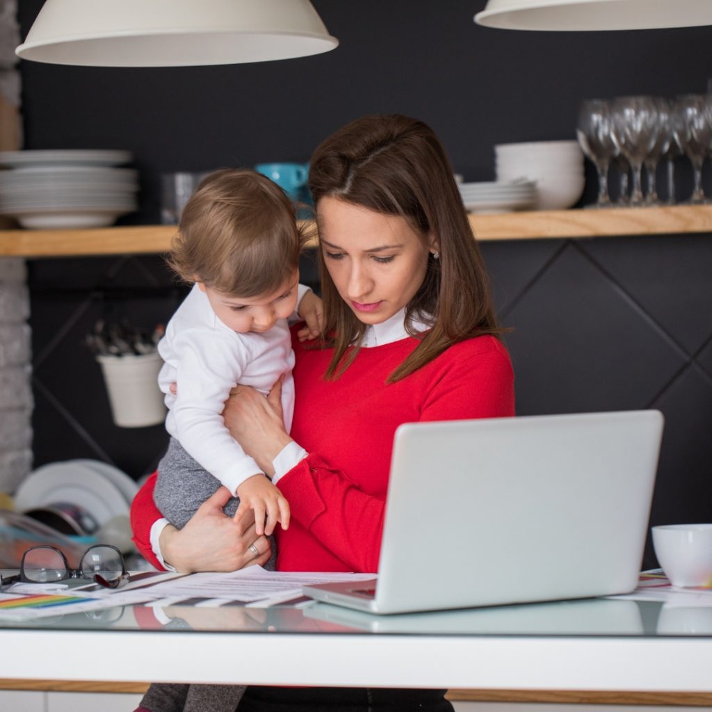 mother working in front of the computer while carrying her toddler child