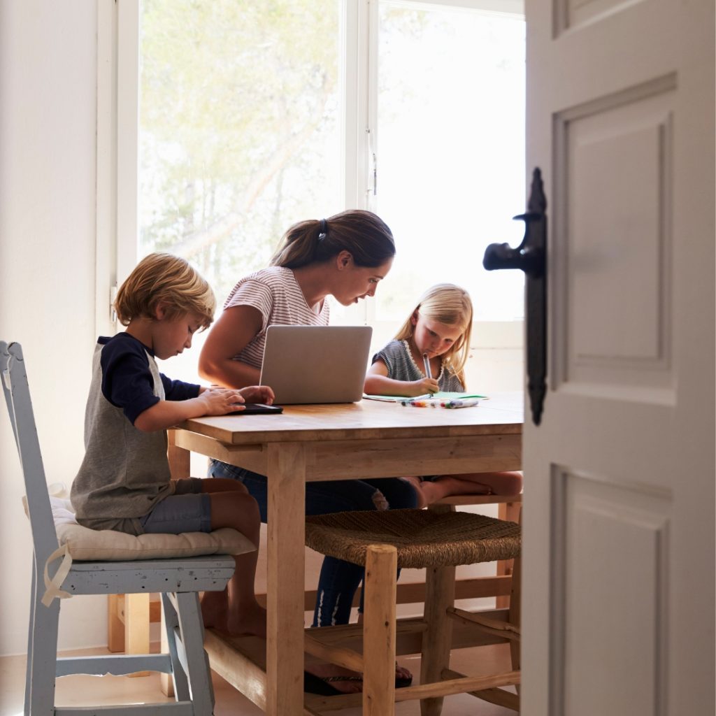a mother is sitting with her children at the kitchen's table, helping them with the school work.
